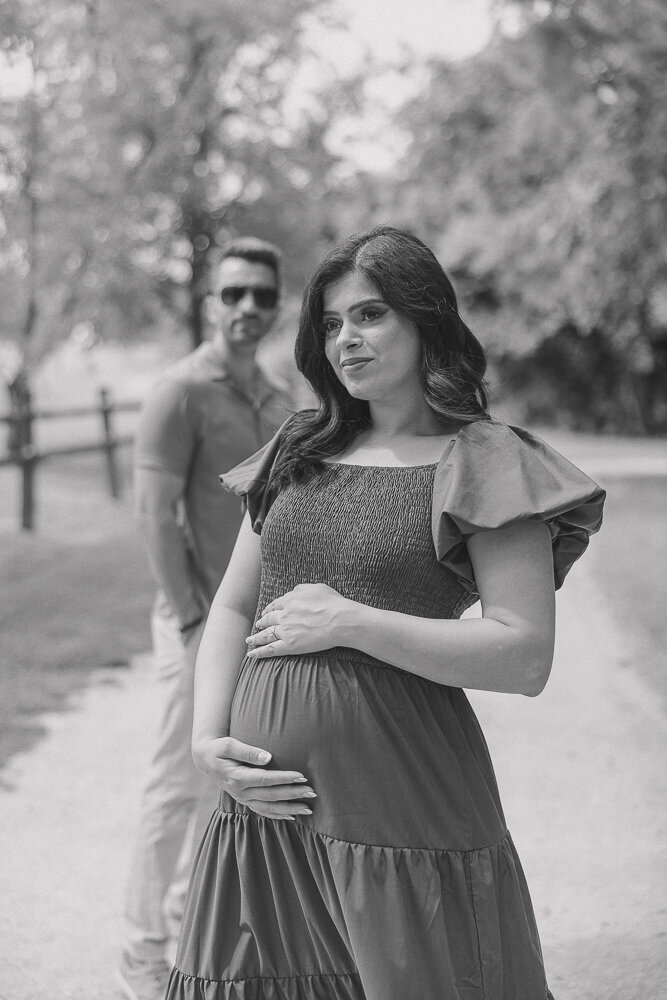 Mom to be smiles towards her bump while her husband stands behind and smiles at her