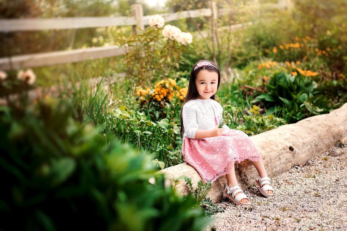 3 year old girl in pink dress surrounded by foliage and yellow flowers