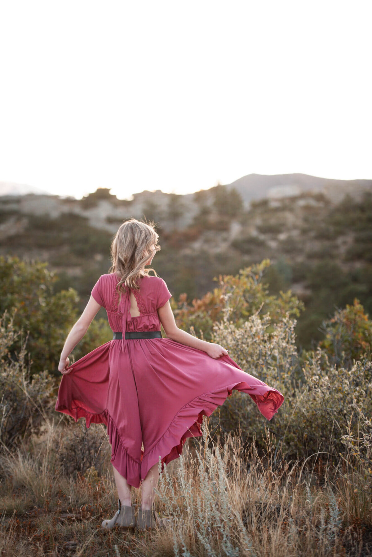 An image from a Denver family photographer of a young girl in a pink dress dancing with her dress in a mountain trail