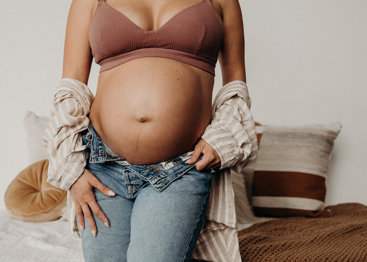 close up pregnancy shot of exposed belly with denim and linen