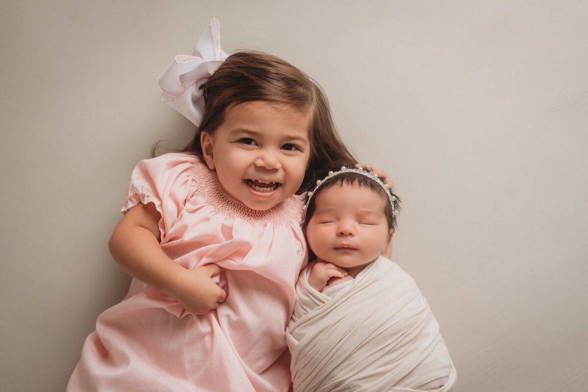 Marietta GA newborn photographer captures big sister and little sister, 20 months old and 2 weeks old laying on backs with big sister holding baby sister
