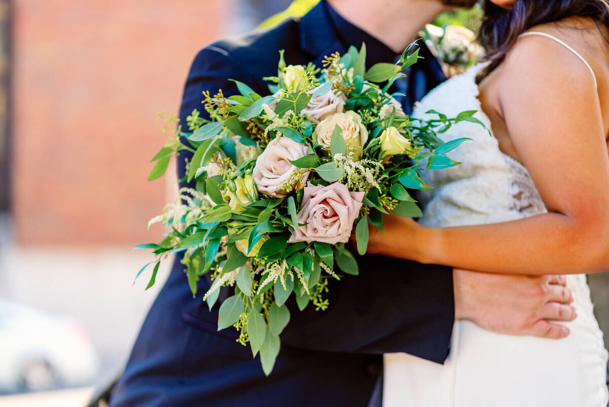 Image of the bride and groom snuggling with the bouquet as the focus. The bouquet has beautiful pink roses.