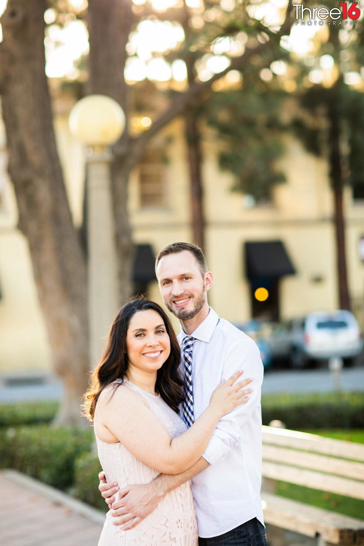 Engaged couple embrace one another and smile for the photographer
