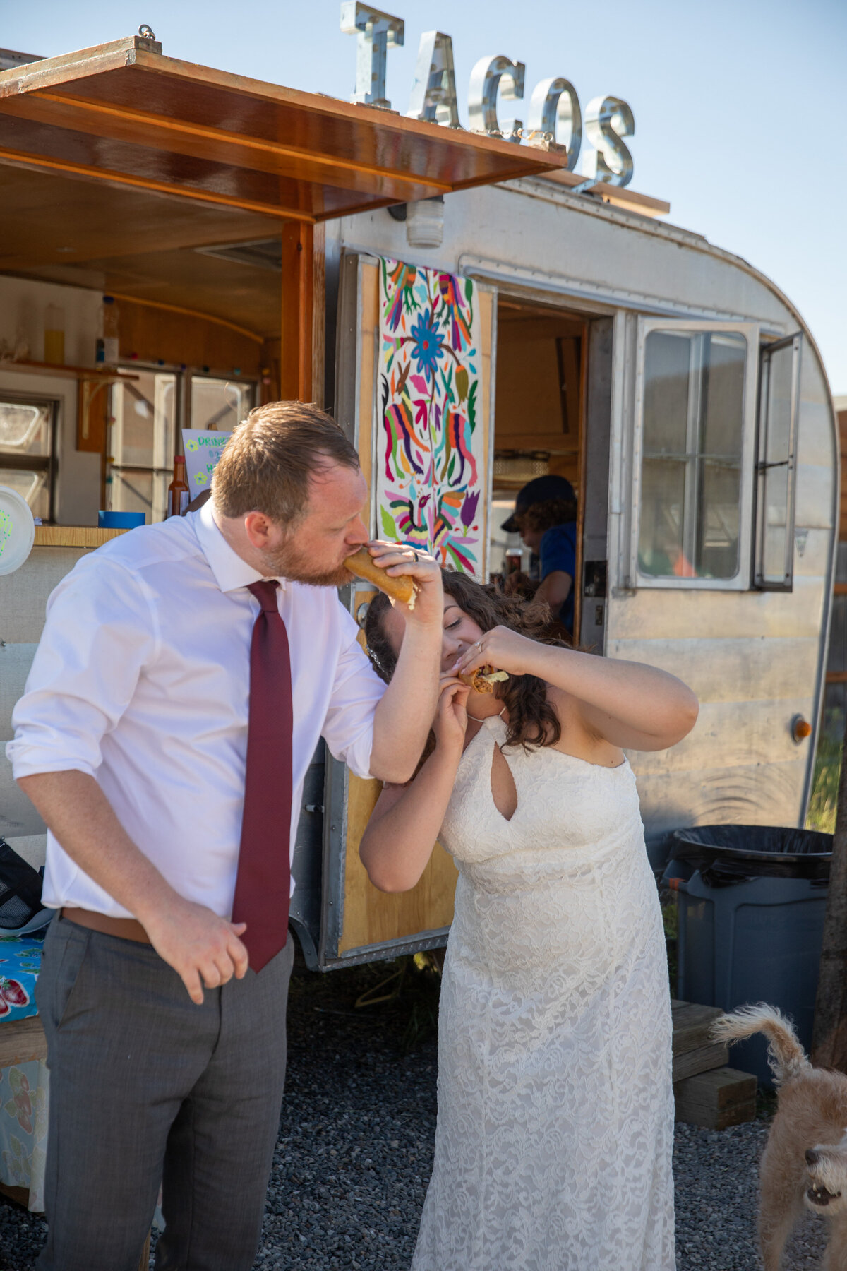 A bride and groom eat tacos on their adventure elopement day while standing in front of a taco truck.