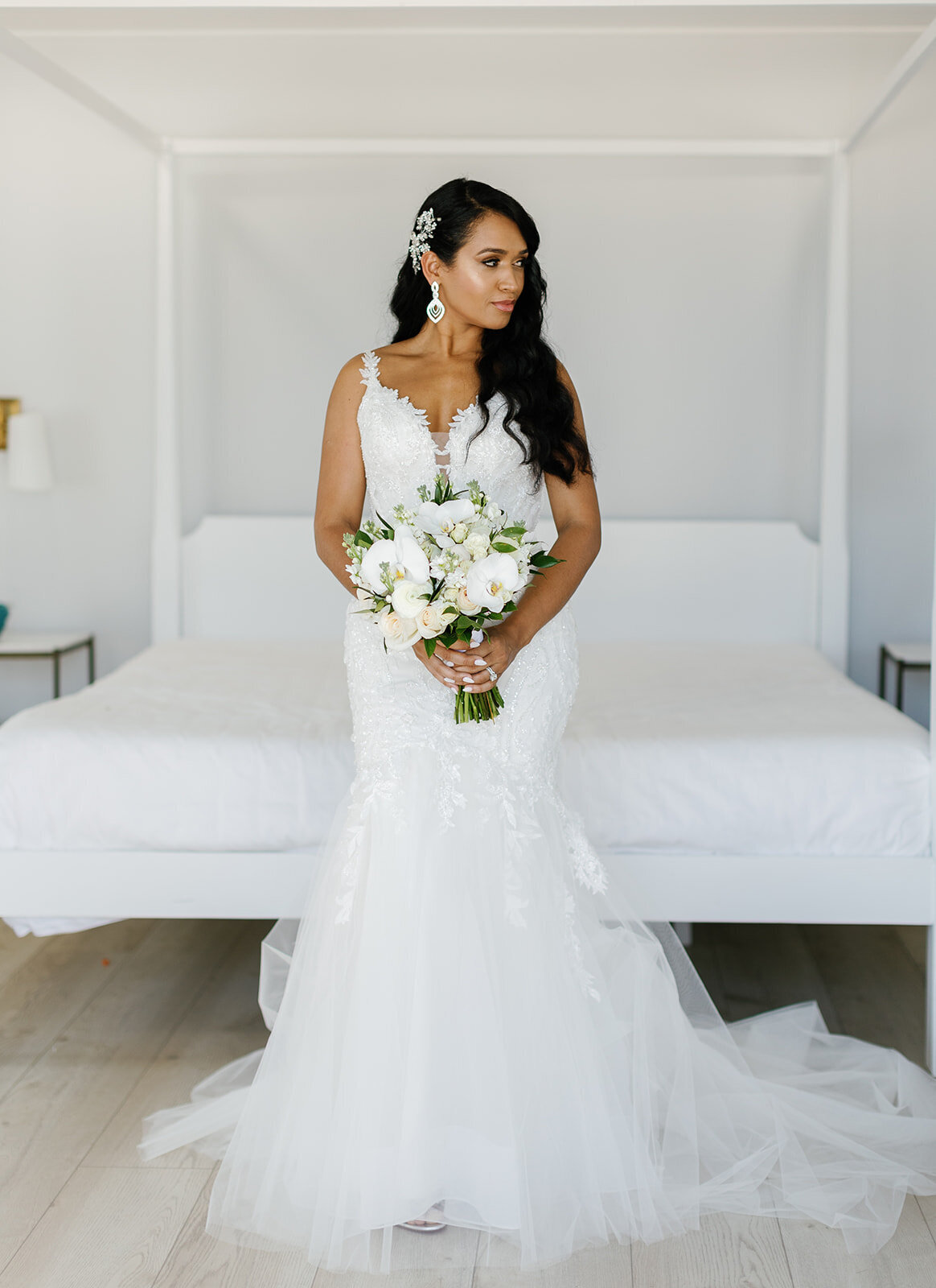 Andressa looks stunning in her lace wedding gown, holding a white floral bouquet while standing in a bright, modern suite at Table Key, Islamorada. Captured by Claudia Amalia, Islamorada wedding photographer.