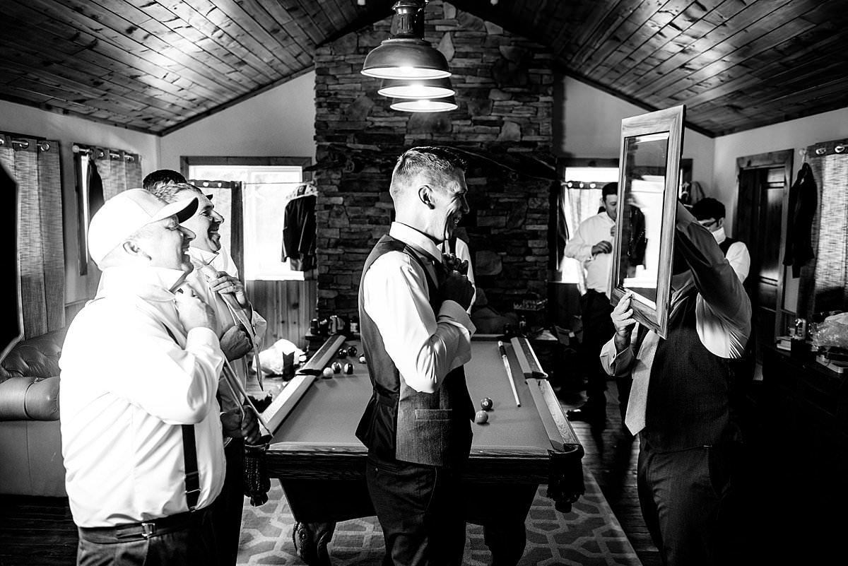 Black and White Photo of groom and groomsmen tying their ties in a mirror held by another groomsman