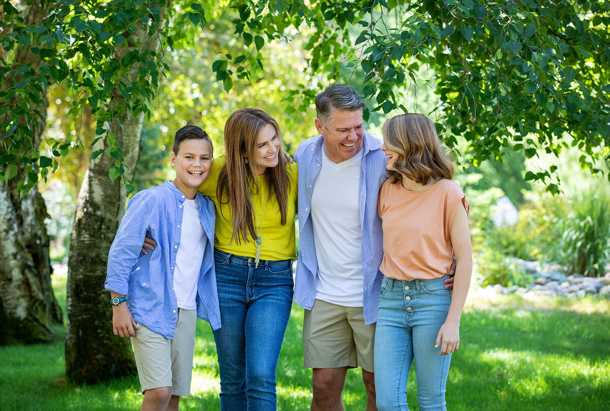 Family of four with two teenagers embracing laughing and hugging.
