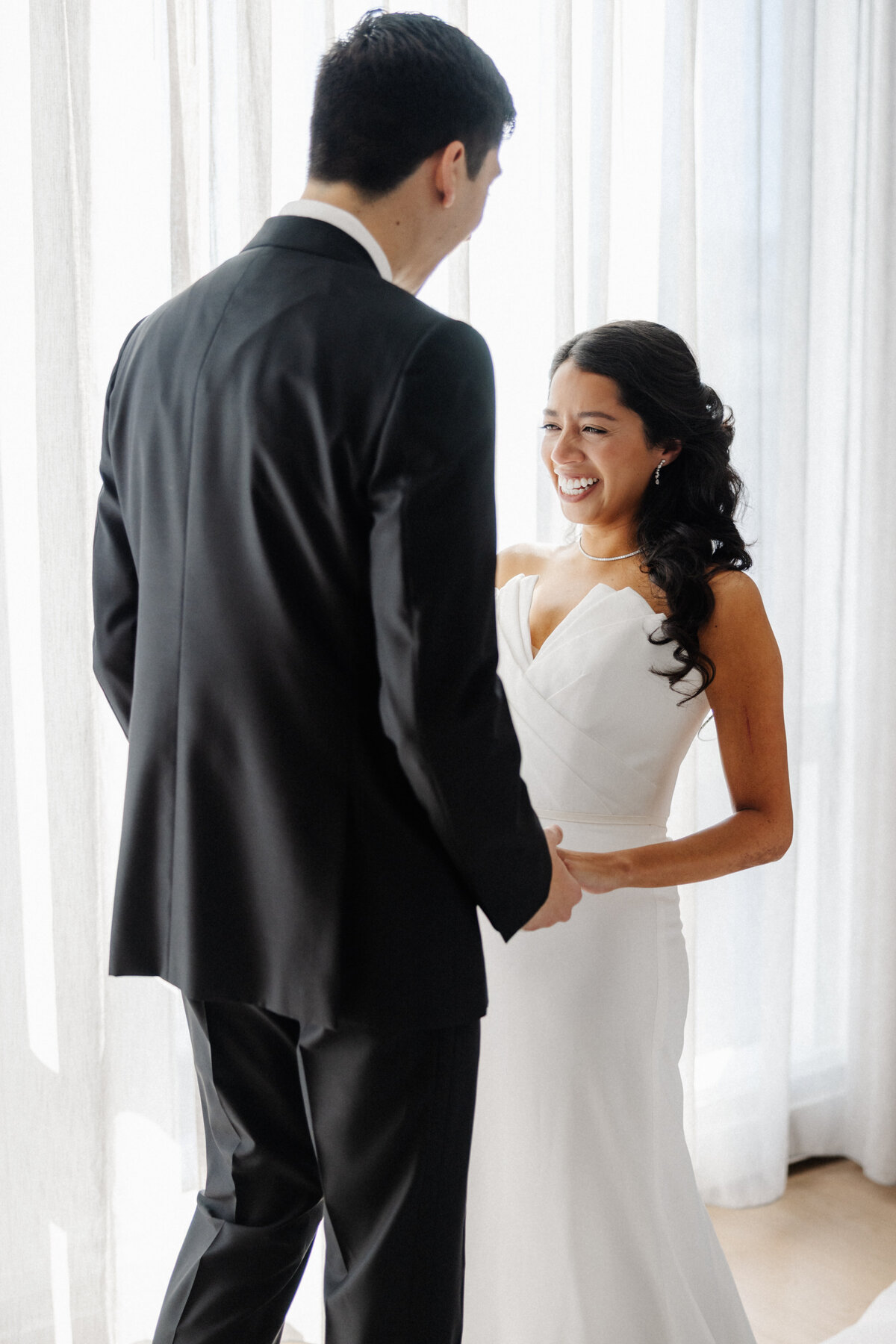 Candid indoor wedding moment of a bride tearing up as she holds hands with the groom.