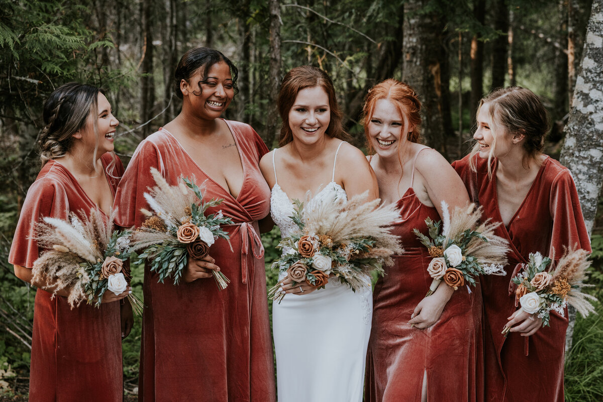 Bride laughs with bridesmaids holding bouquets.