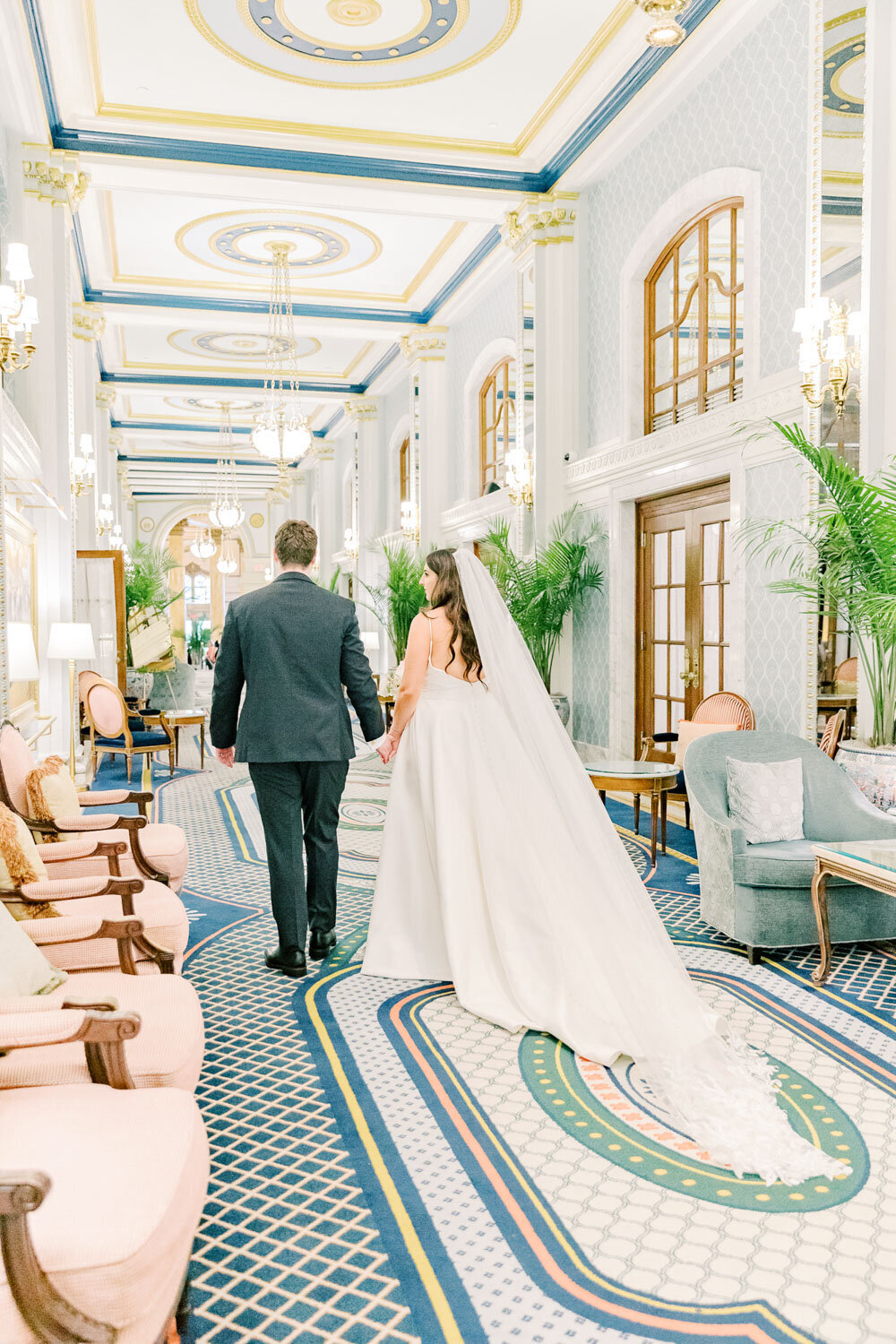 Bride and groom walking hand in hand in elegant hallway.