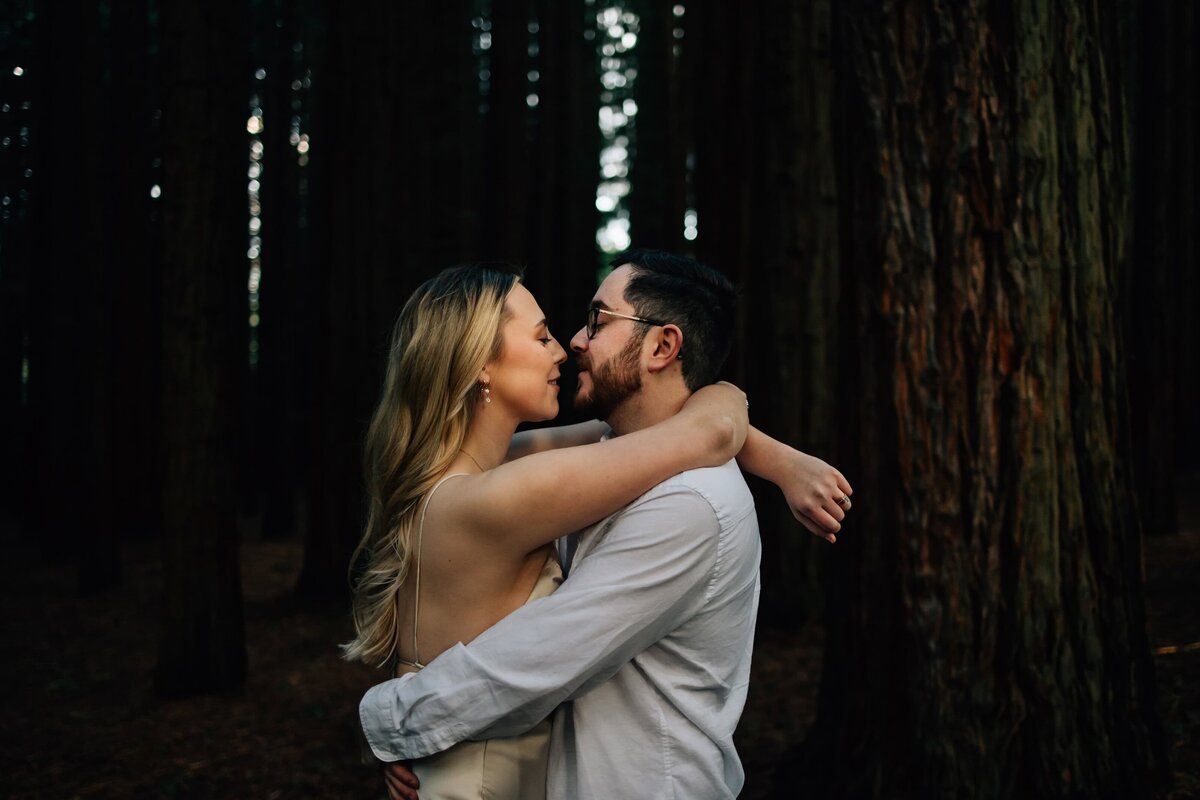 Engagement photoshoot image of couple with arms around each other in forest
