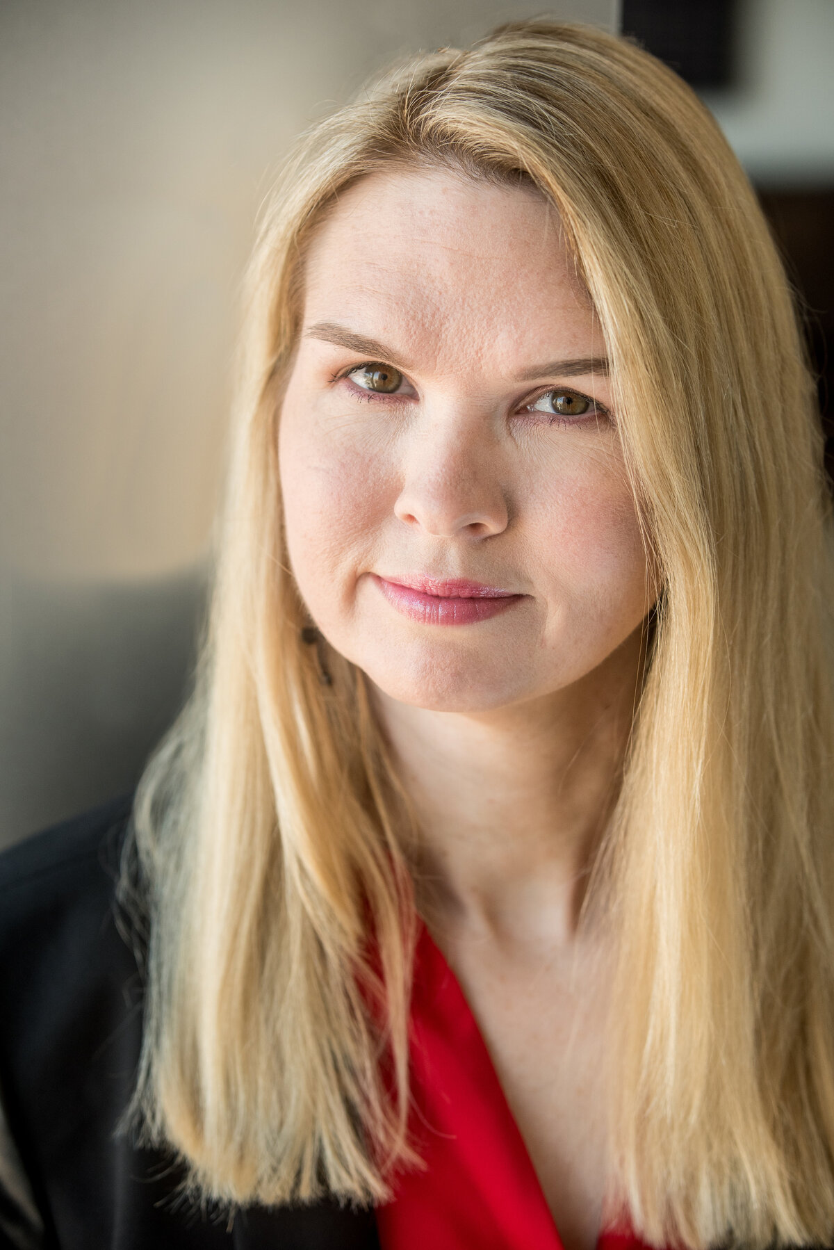 a woman with blonde straight hair looks at the camera, wearing red and black