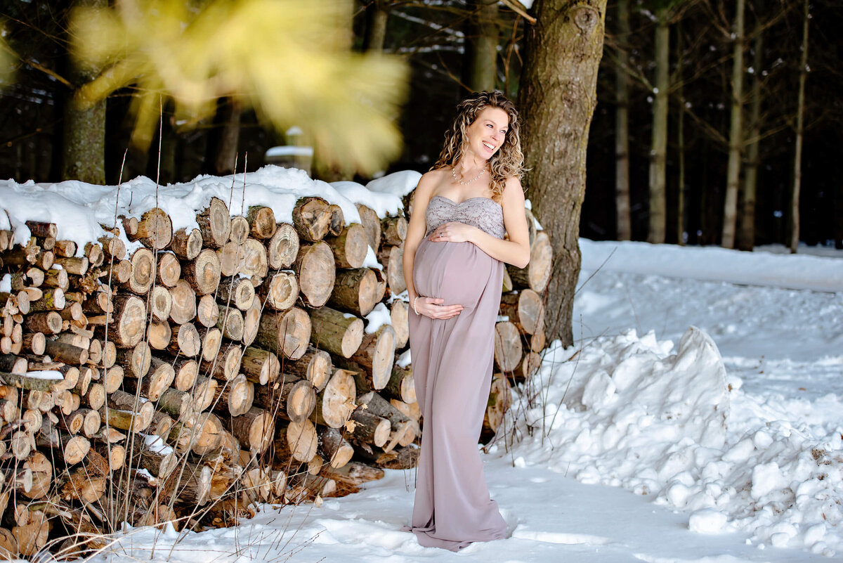 Pregnant woman wearing a beige maternity dress in the snow for her outdoor Burlington, ON maternity photos