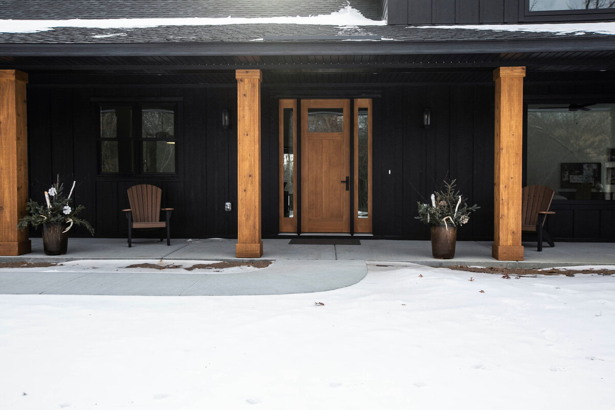 Exterior view of custom home in Elk River, Minnesota with black siding, wood details and front porch built by Cornerstone Custom Builds