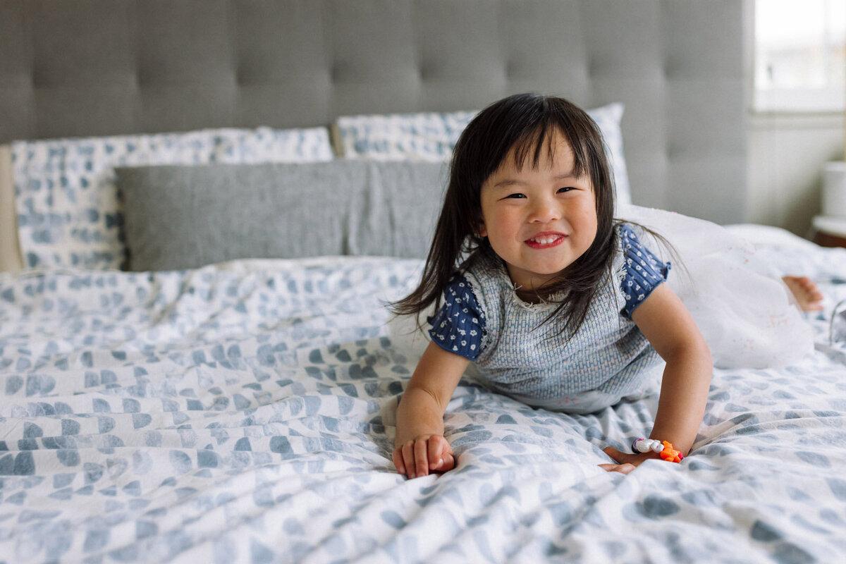 girl laying on bed with patterned blanket looking at camera and smiling