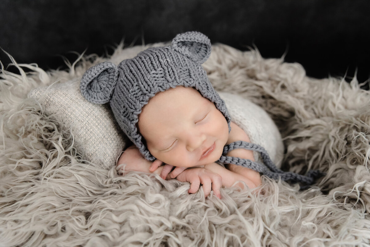 baby boy with gray teddy bear hat sleeping on belly on gray fur