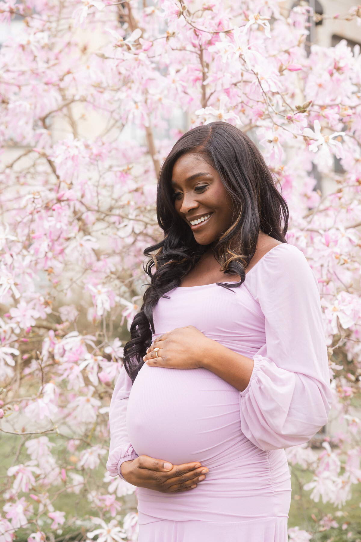 A peaceful solo moment as the mom-to-be gently looks down at her baby bump, standing amid the cherry blossom trees at the University of Washington campus, embracing the beauty of this special time.