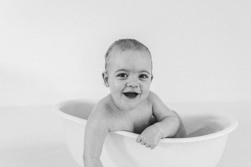 Baby booy in a mini bath leans out and smiles