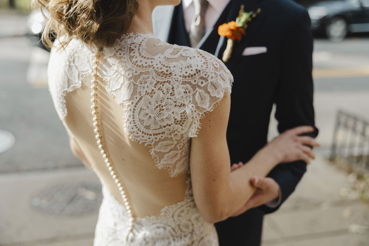 Close up showing the detail of the back of a wedding dress on a person standing with their partner 