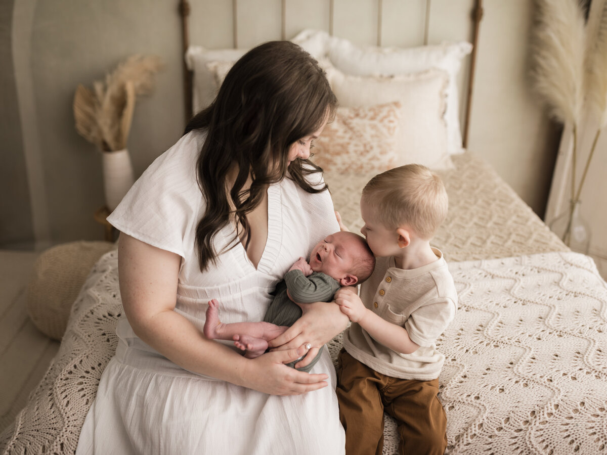 mom in white dress and son holding newborn baby boy in green onesie cleveland newborn photographer