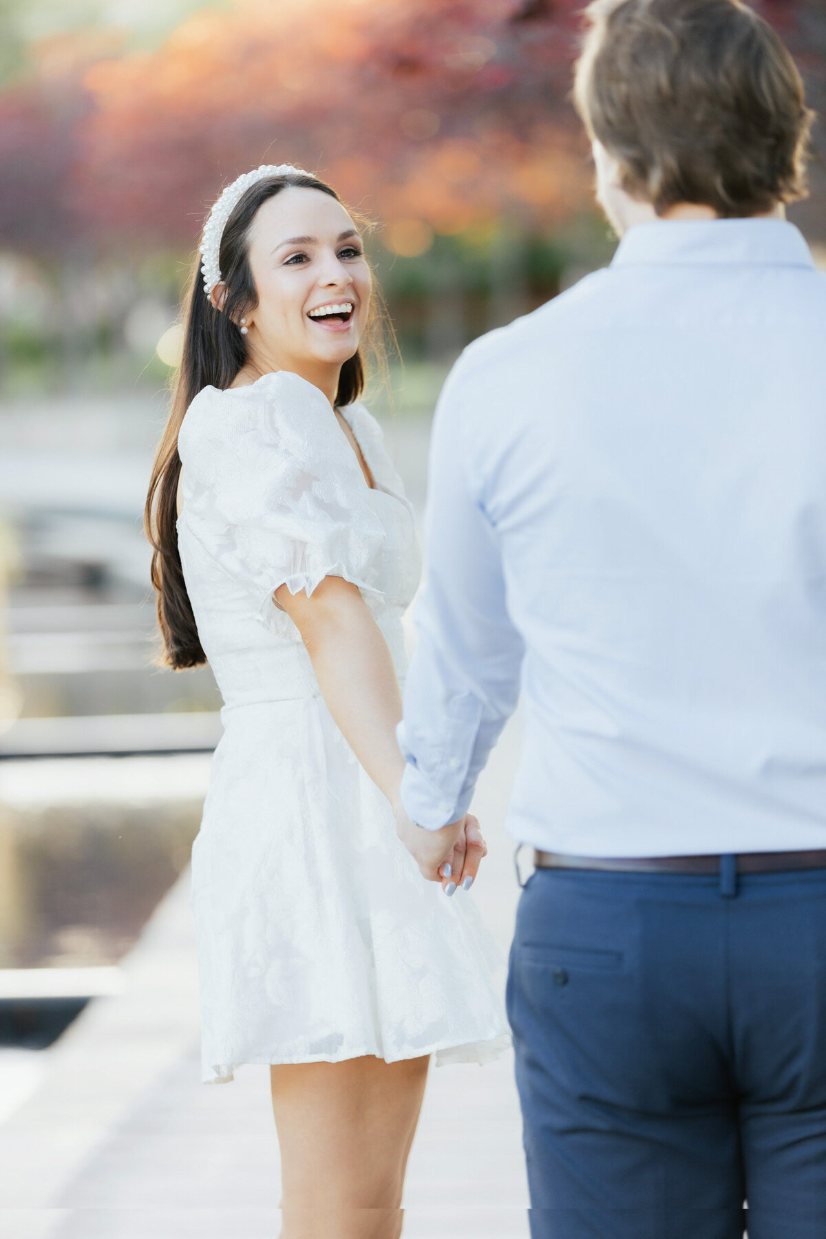 Close up of a woman walking and looking back at her fiancé, laughing candidly during their Lewisville Ferguson Plaza engagement session.