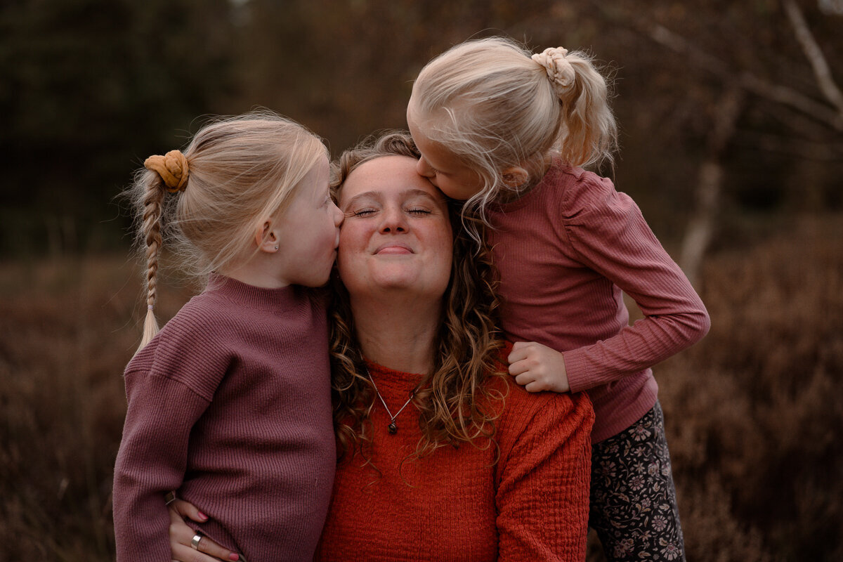 Moeder krijgt vaan haar twee dochter een kus op allebei haer wangen.