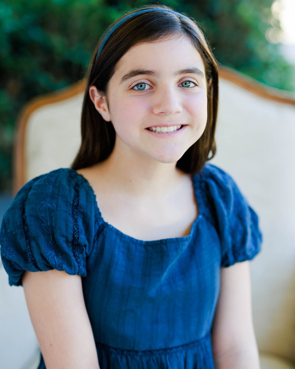 Outdoor headshot of a young girl sitting in a chair.