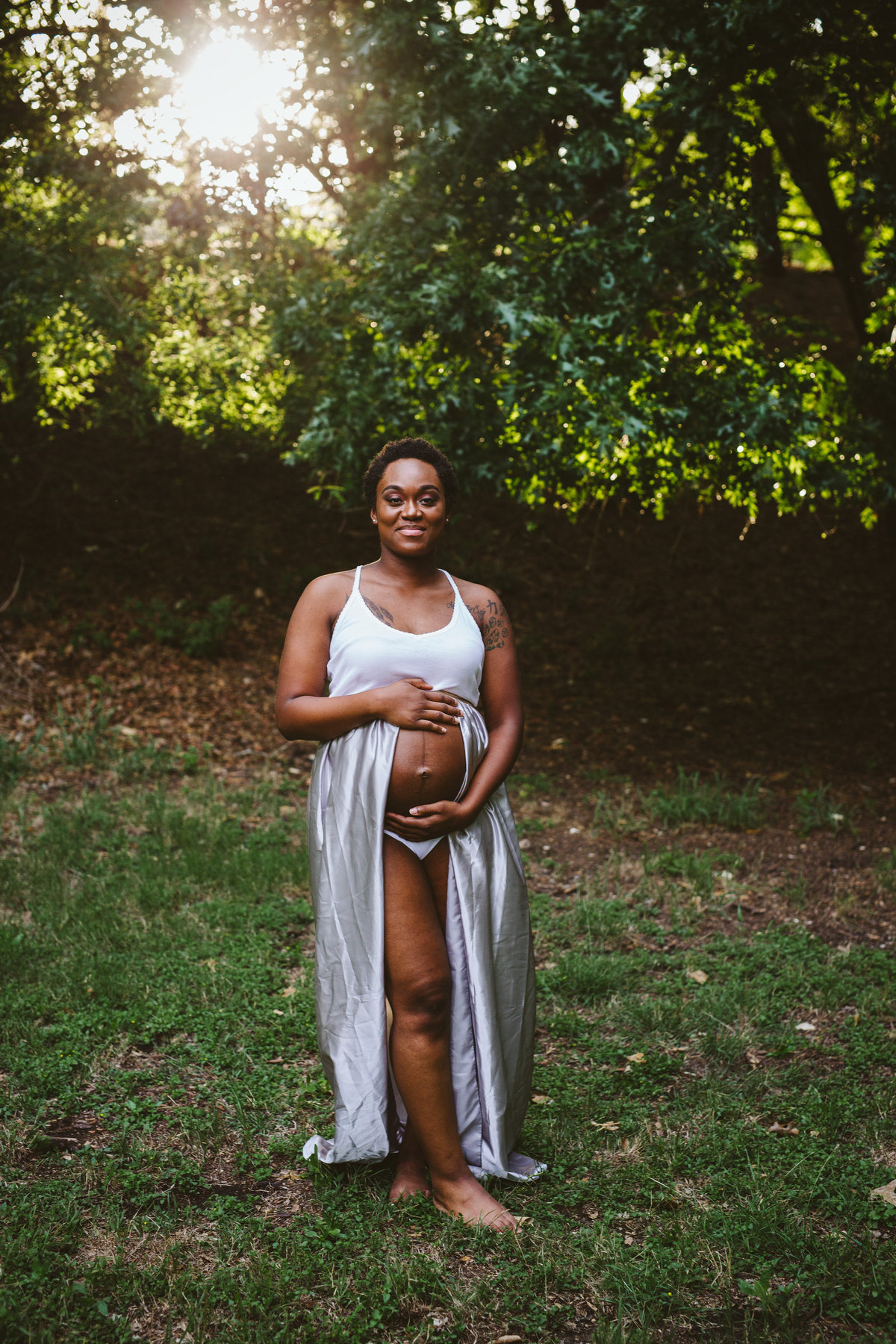 Maternity session of expecting mother holding her belly and posing in a clearing at Denman Estate Park in San Antonio