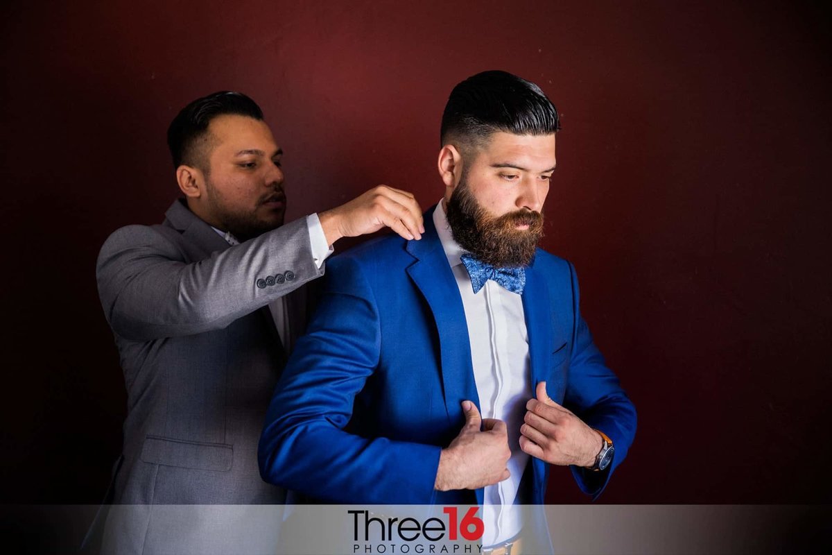 Groom gets help putting on his royal blue suit coat