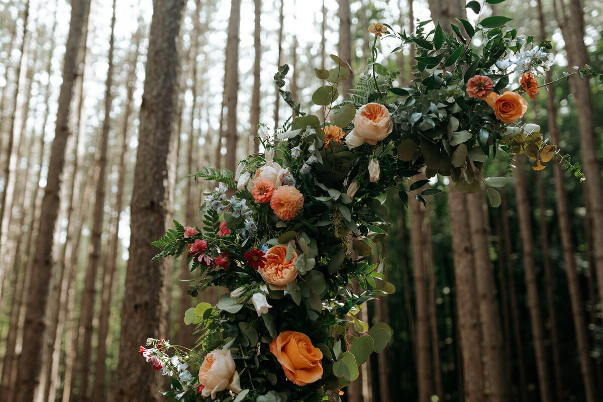 Detail of a woodland wedding arch with peach and orange roses and pops of blue delphinium