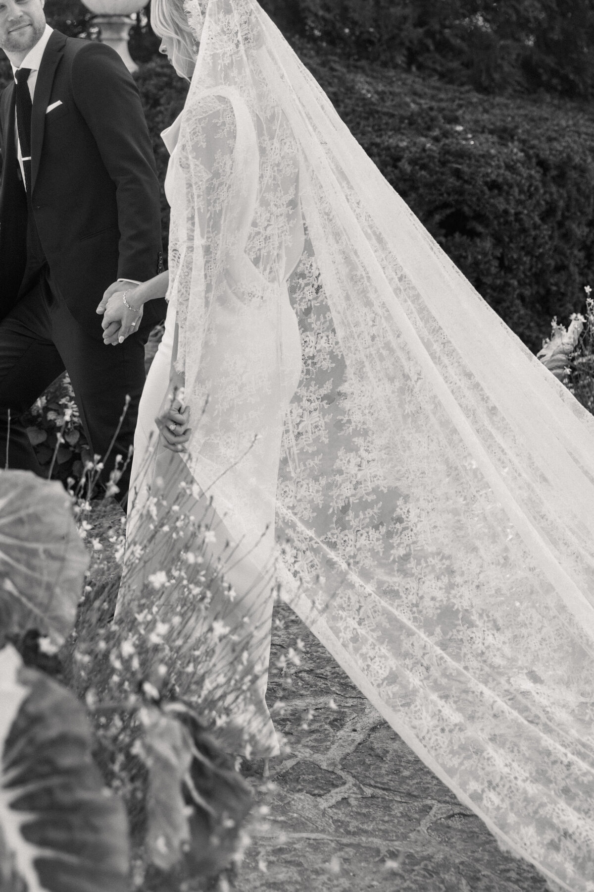 Black and white photo of bride’s lace veil detail, walking garden path at Dayton wedding.