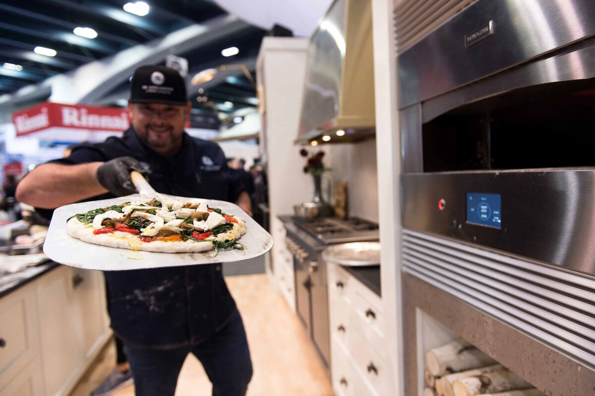 A Chef holds a handmade pizza close to Monogram pizza oven at PCBC home builders convention in San Francisco