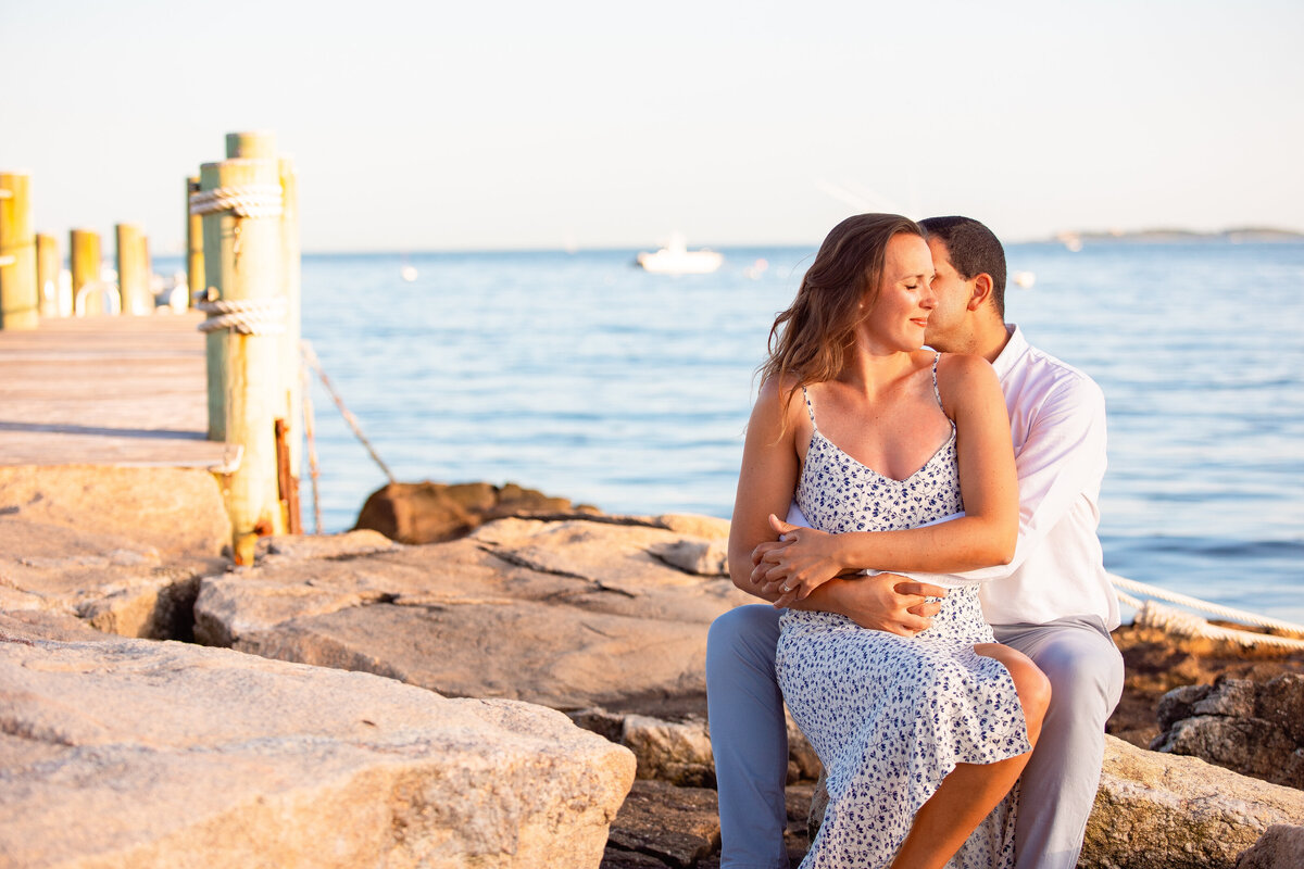 Man hugs fiancé as she smiles during their engagement session in Stonington, CT.