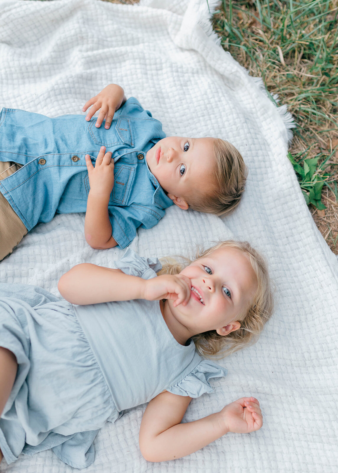 Brother and sister laying on blanket on the grass