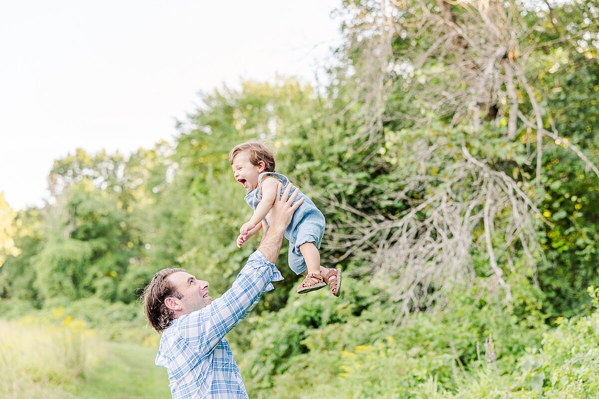 father holds son up high during Family photo session with Sara Sniderman Photography at Heard Farm in Wayland Massachusetts