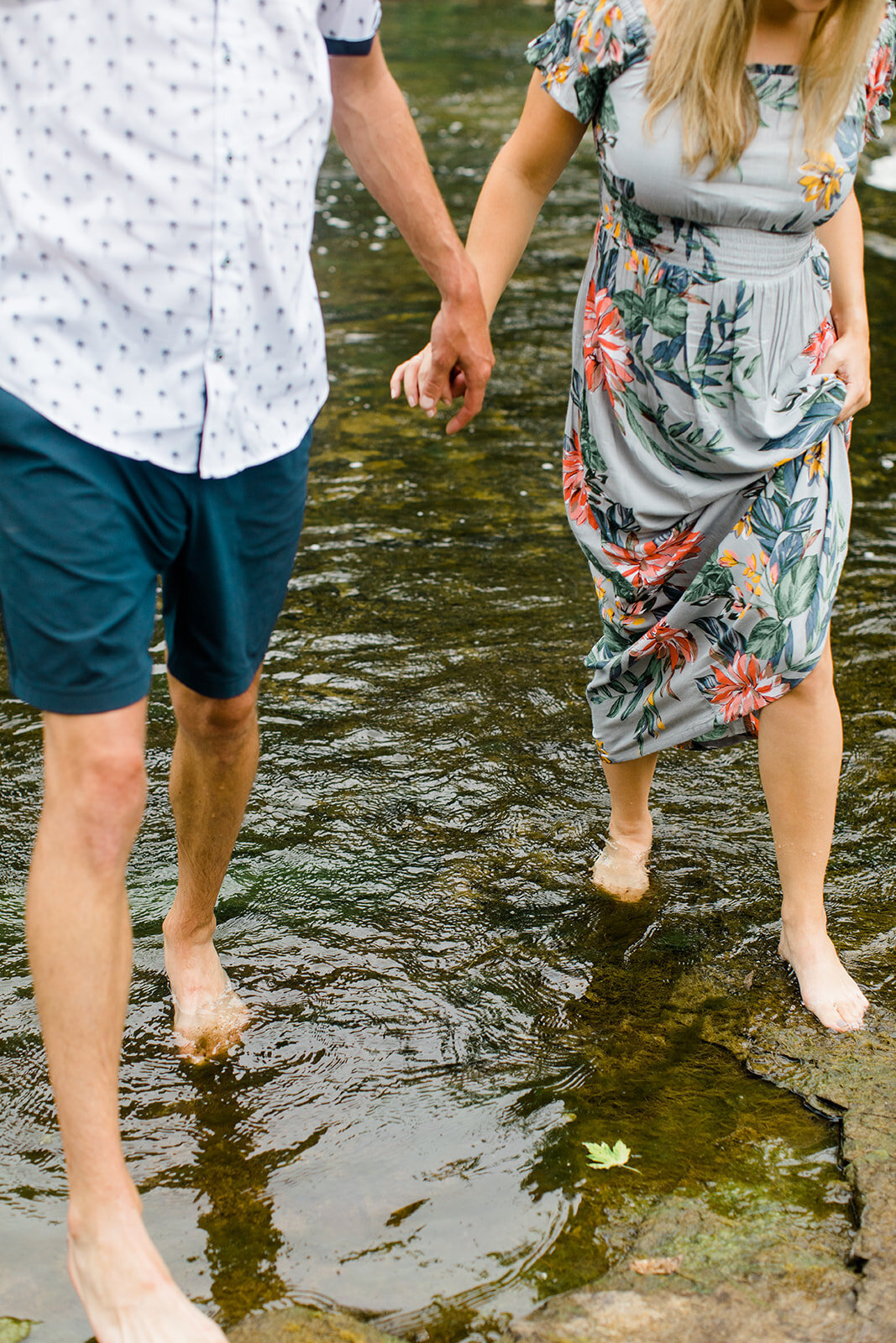 man and woman walking barefoot though a river while holding hands