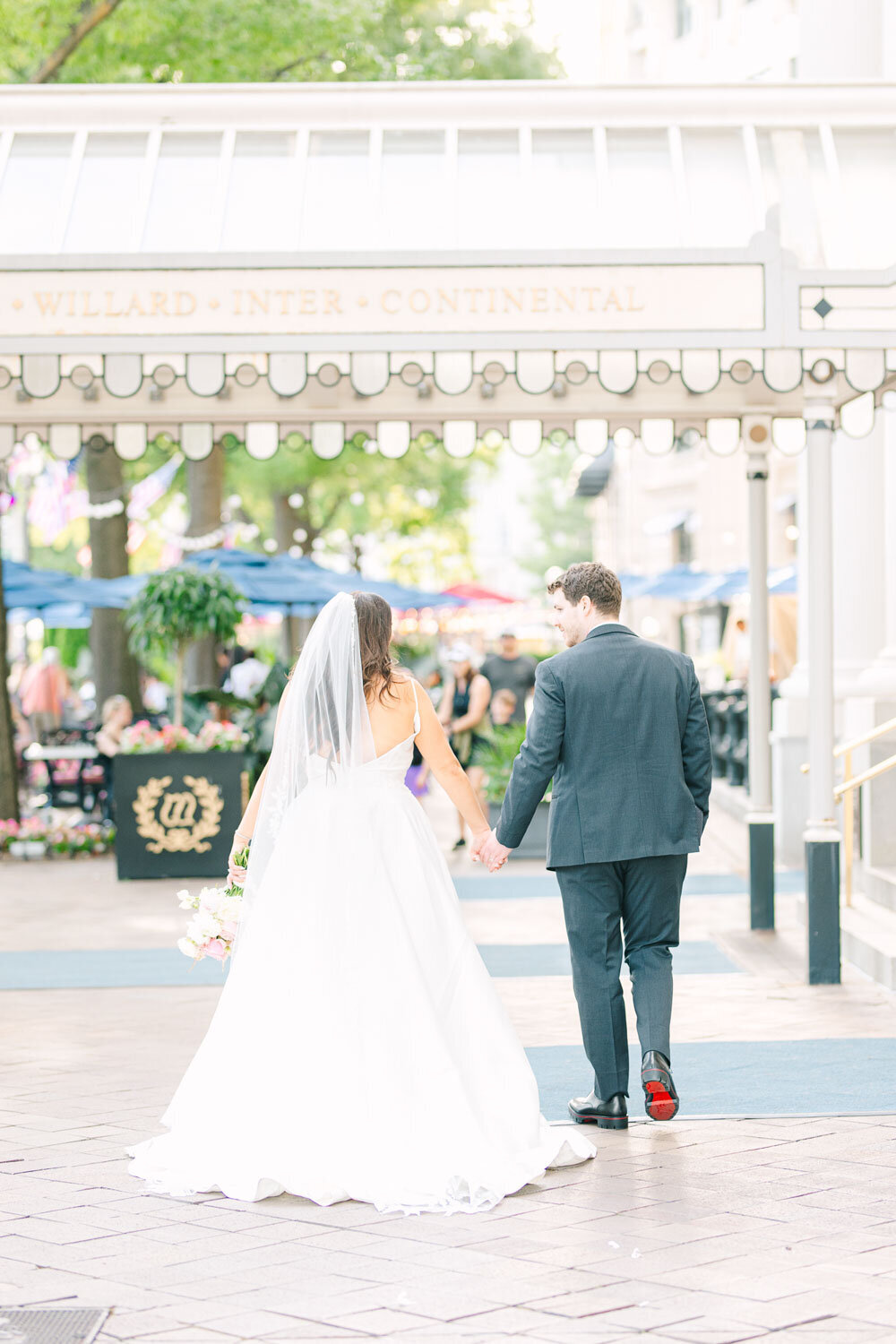 Bride and groom walk hand-in-hand under hotel canopy