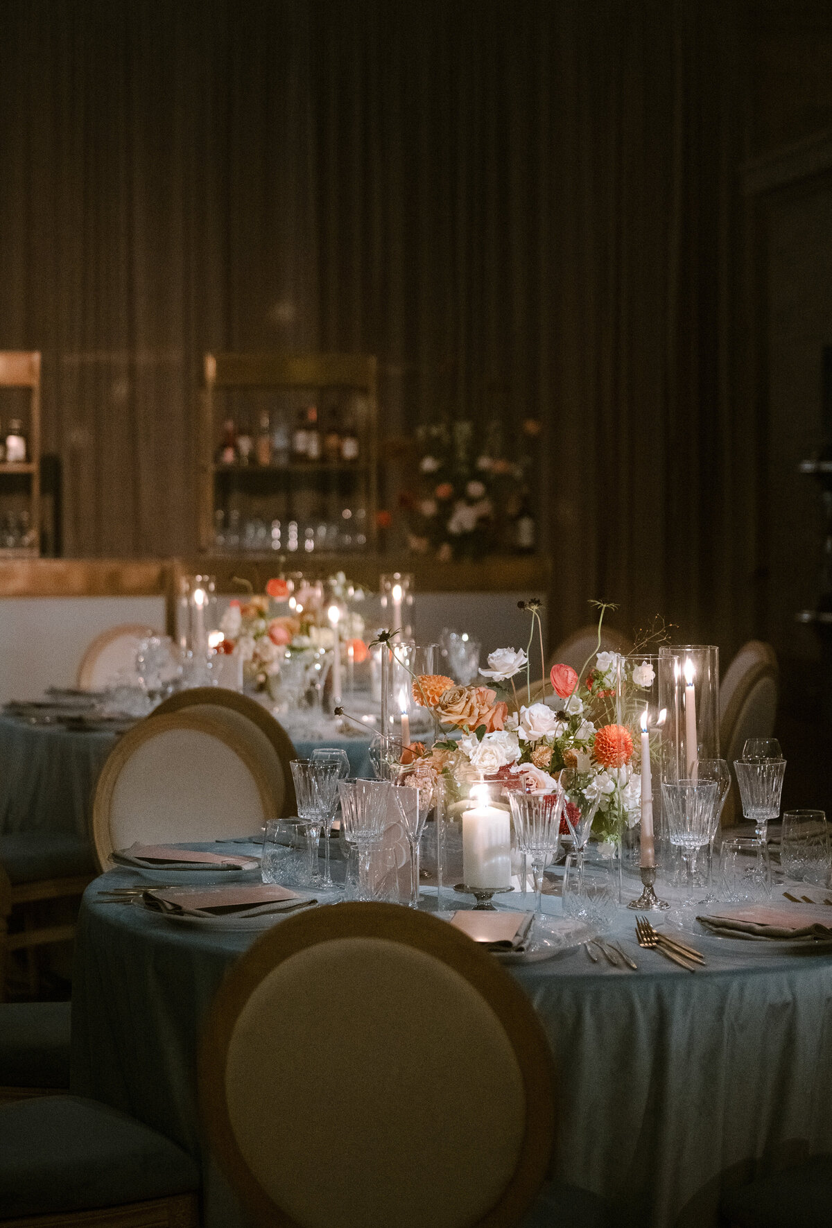 Cozy tables at Theatre St James decorated with candles and garden floral centrepieces on blue tablecloths.