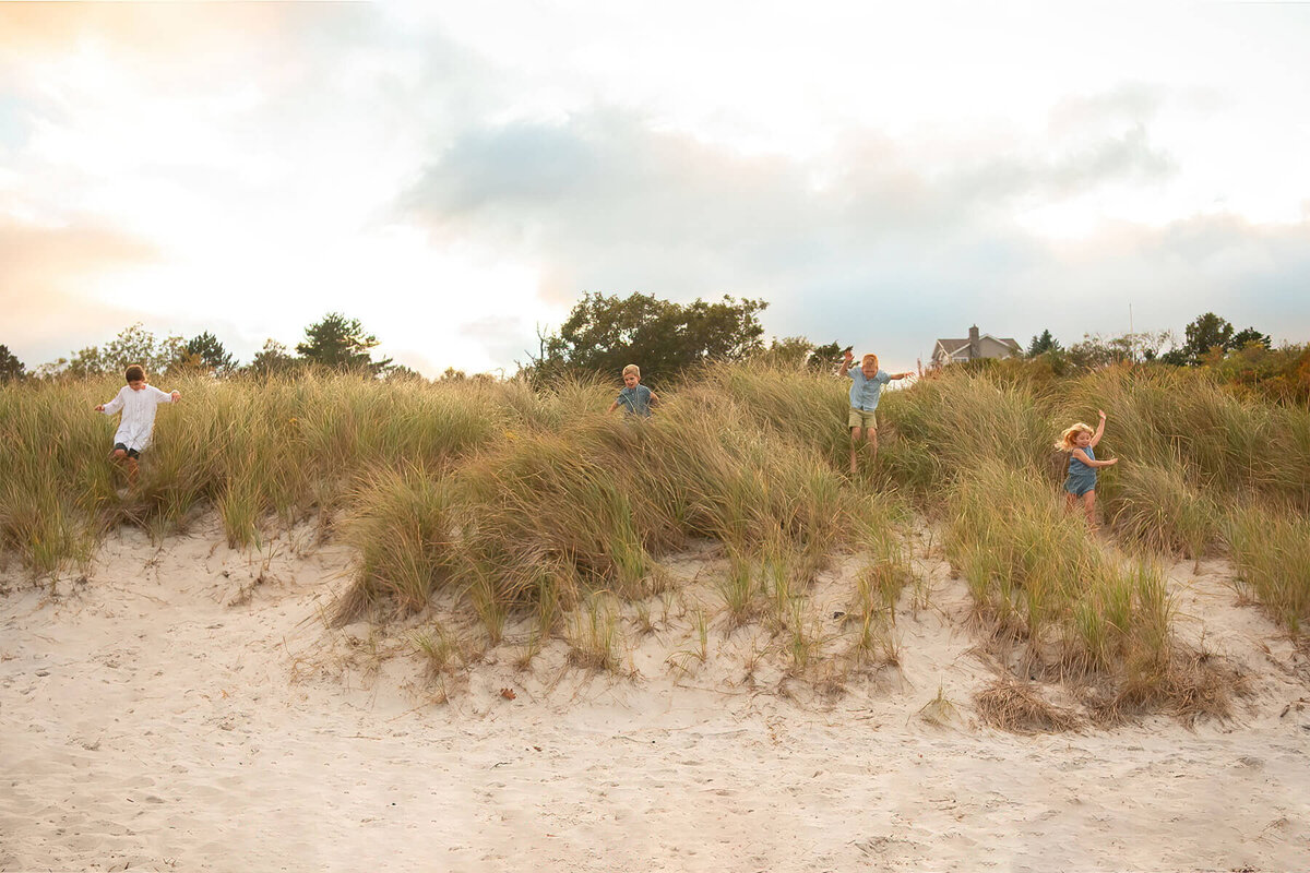 Four children run down a sandy bank at Wingaersheek Beach.