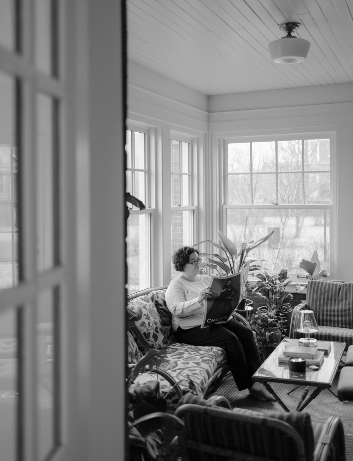 web designer reads newspaper in sunroom with plants, ALEO Detroit, Little village