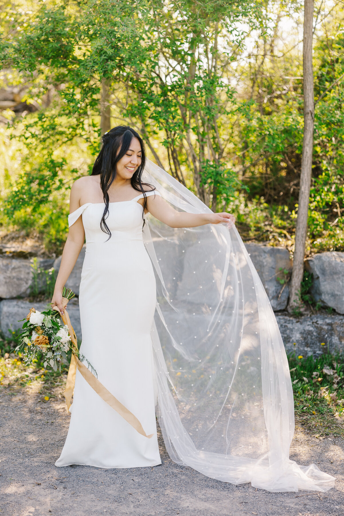 Bride holding out her veil while posing outside