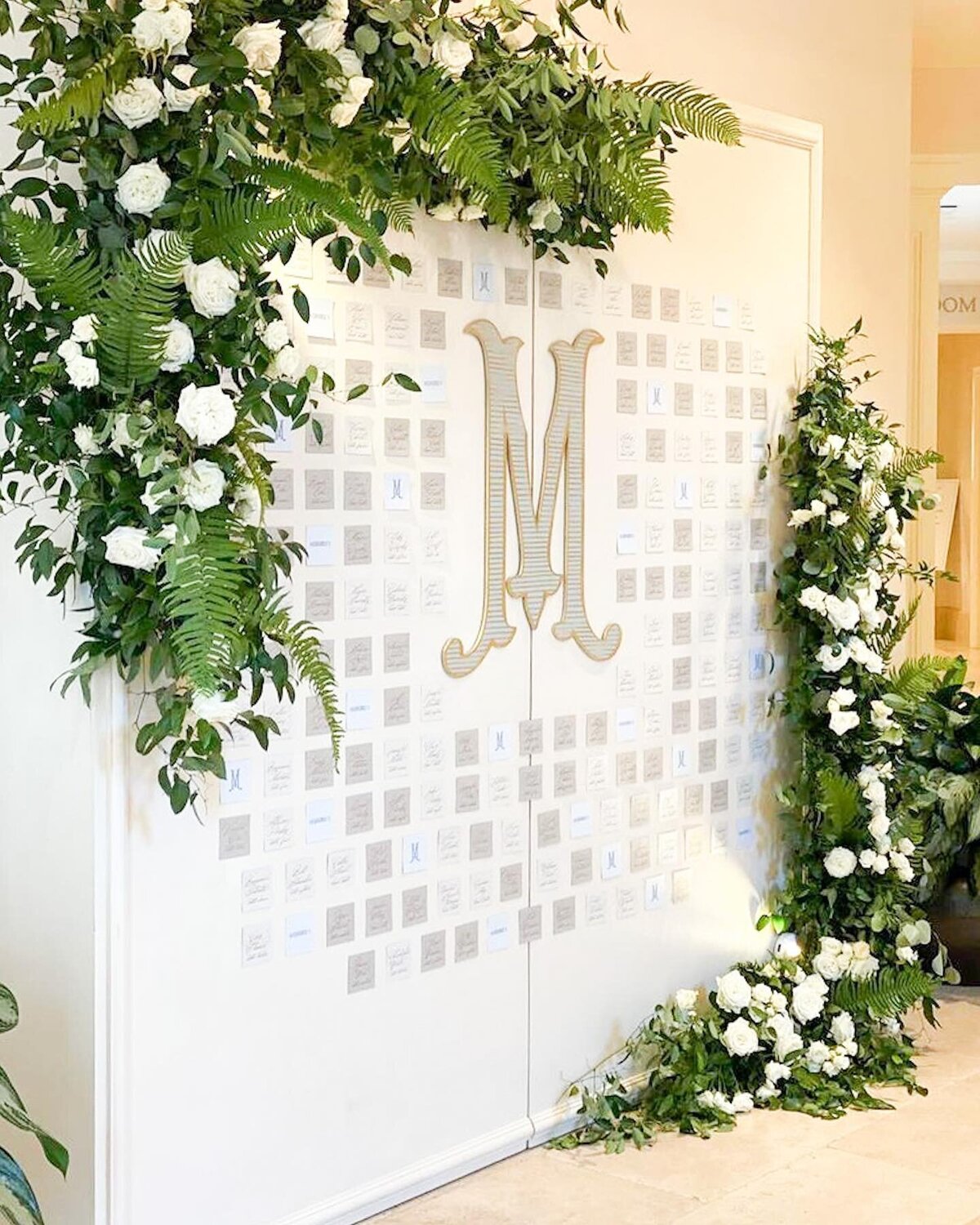 White wedding backdrop with large monogram letter decorated with white florals and greenery