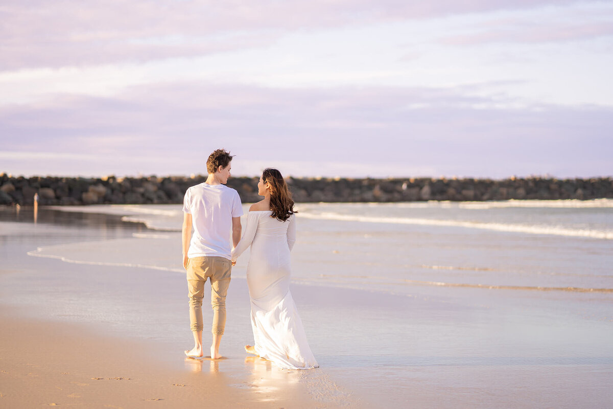Couple walking along purple sunset beach having maternity photography done in Gold Coast