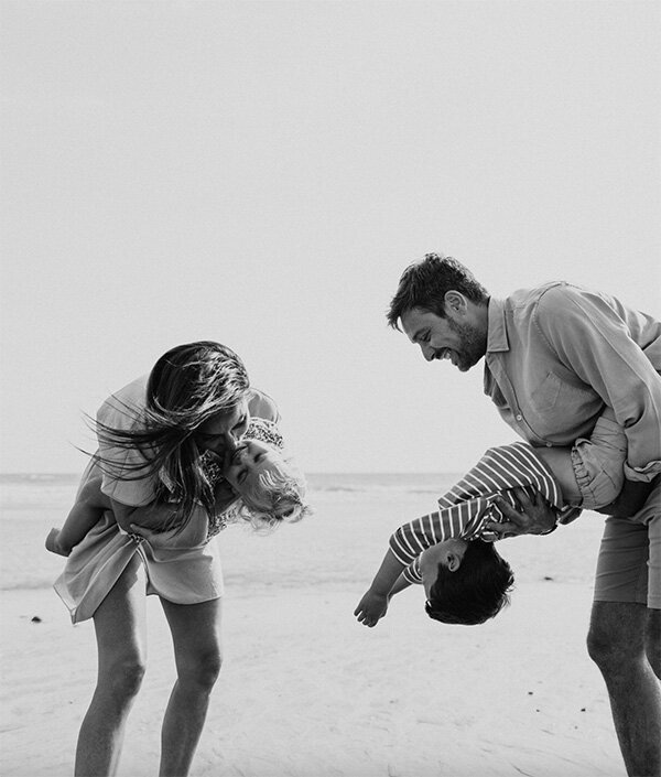 Parents faisant faire des pirouettes à leurs deux enfants à la plage. Scène immortalisée en noir et blanc par Laura Termeau photographie.