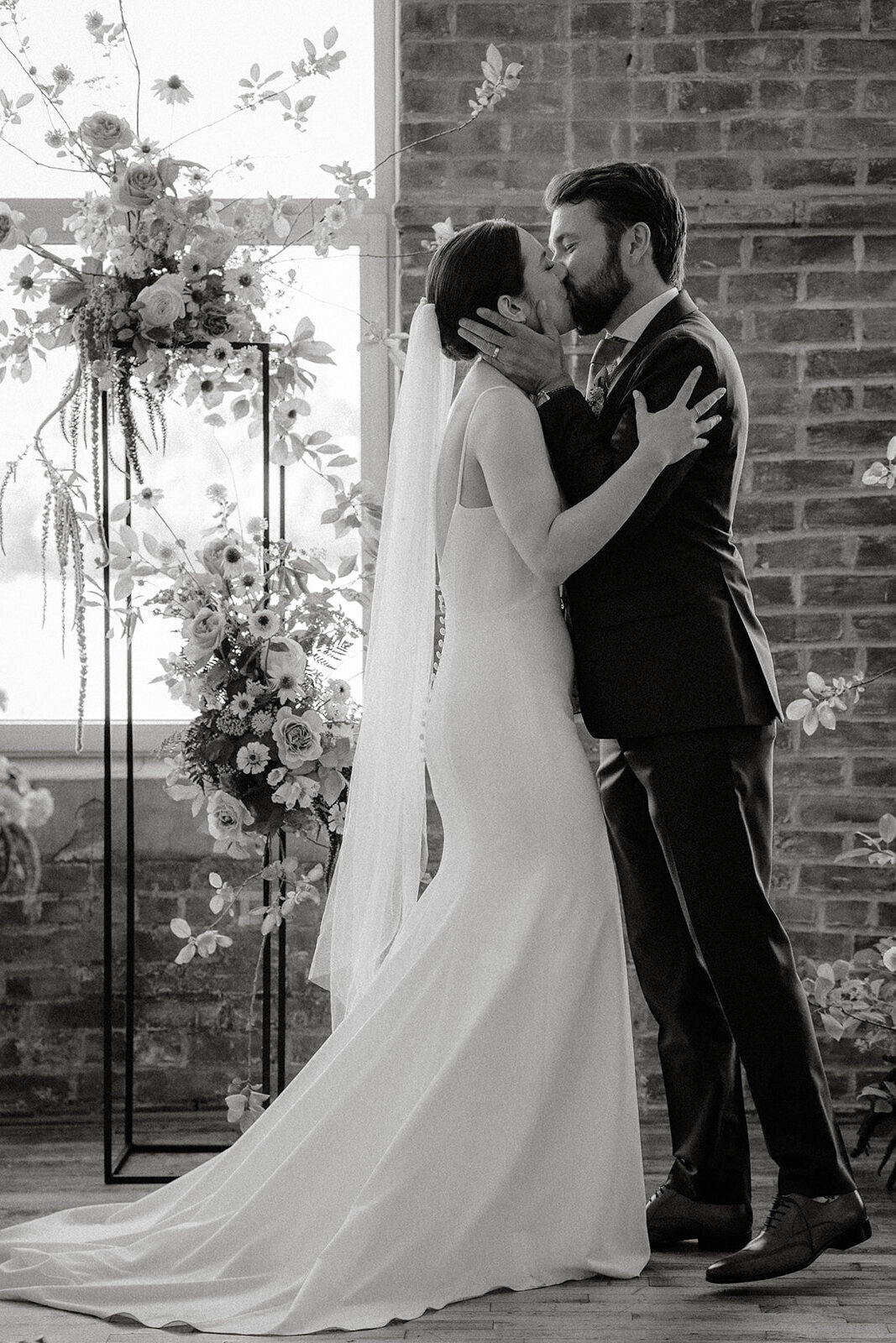 A couple kiss in front of a flower arch at a rustic chic wedding ceremony Entrepot Dominion. 