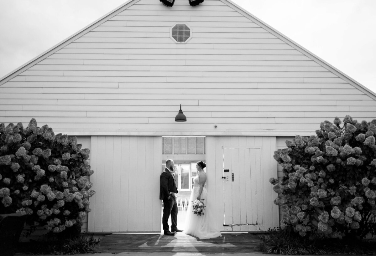 black and white wedding photo with bride and groom standing on either side of an open barn door at Sunny Slope Farm as the light from the building floods out the door frame