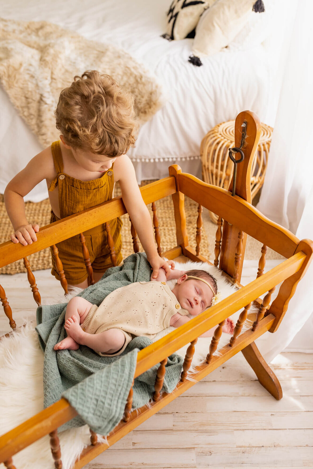 Big brother rocking his baby sister in a an antique wooden bassinet