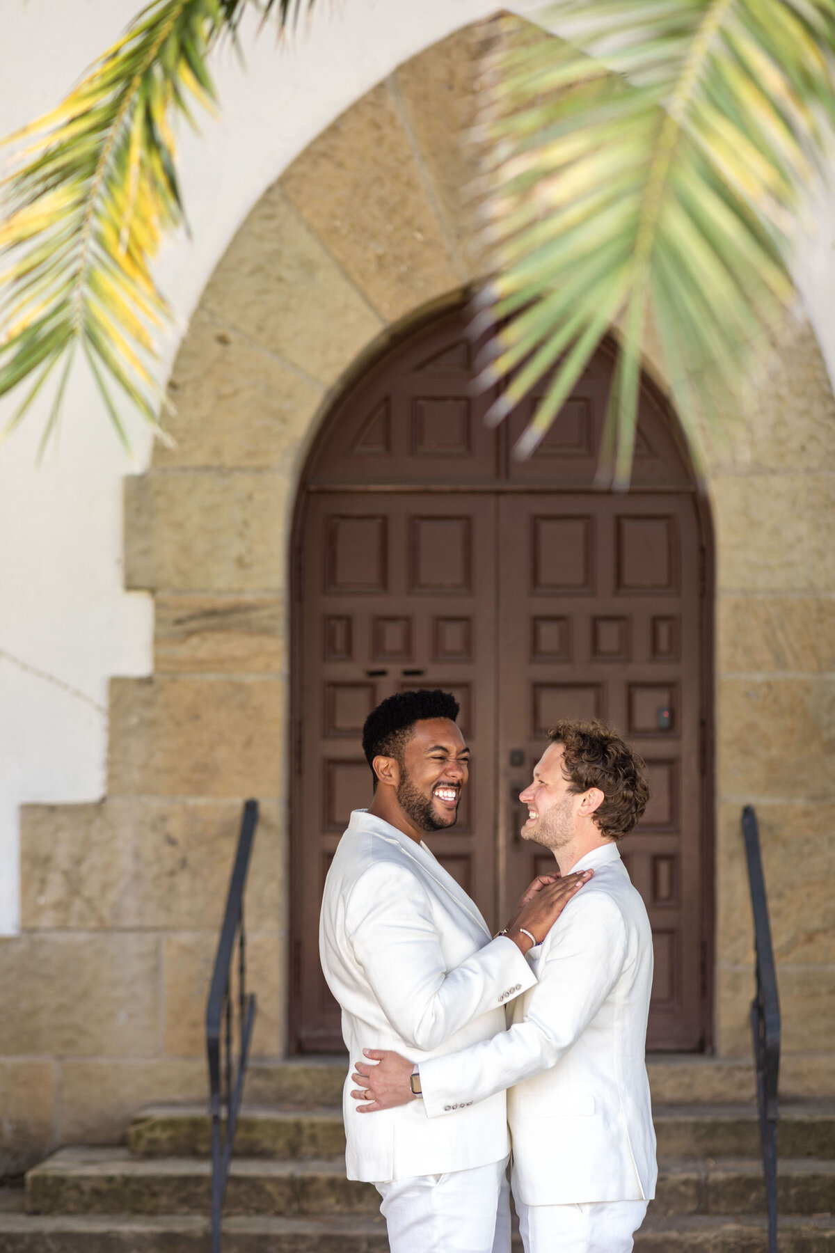 A couple standing outside a large arched door smiling.