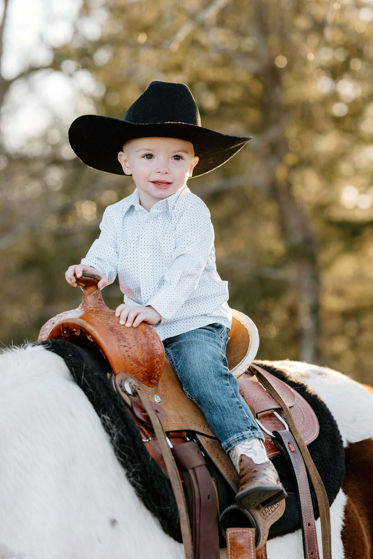 two year old boy in western clothes, boots, and cowboy hat sitting on horse