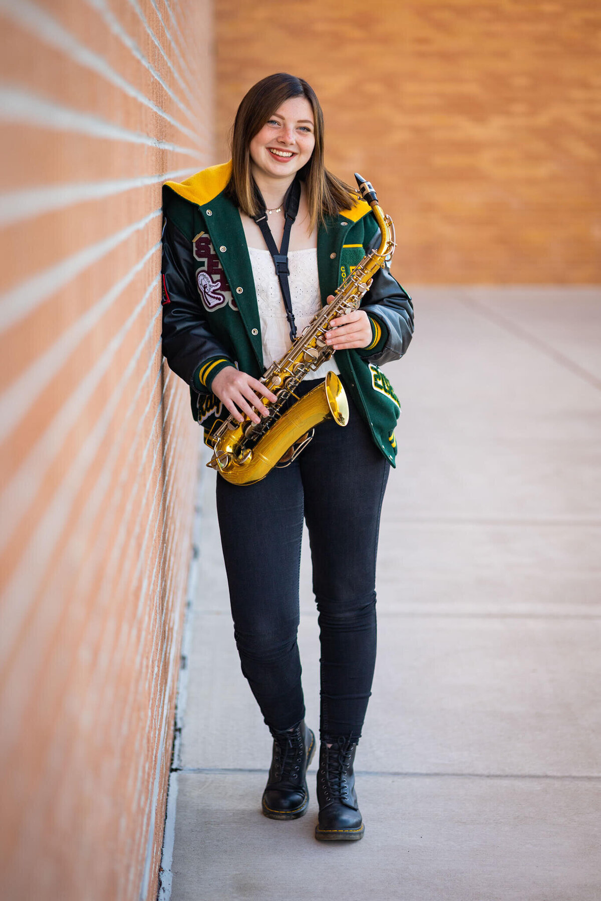 high school senior holding her saxophone leaning against a brick wall